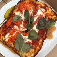 Rectangular pizza with basil, pepperoni, and a side pepper in a box.