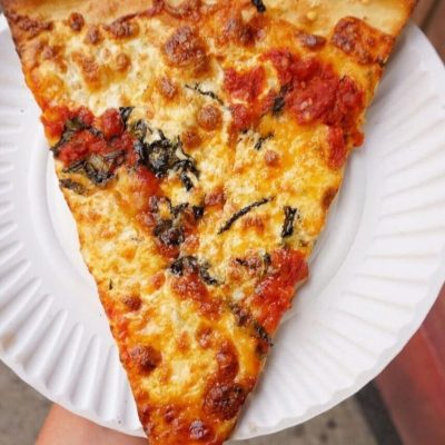 A slice of pizza with cheese and tomato sauce on a white paper plate.
