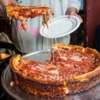 Person serving a slice of deep-dish pizza with melted cheese on a white plate.