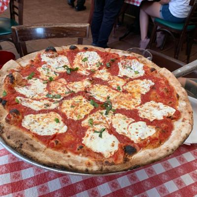 Large pizza with tomato sauce and cheese on a checkered tablecloth in a restaurant.