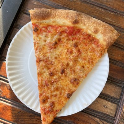 A slice of cheese pizza on a white paper plate on a wooden table.
