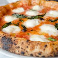 Close-up of a margherita pizza with basil and melted cheese on a plate.