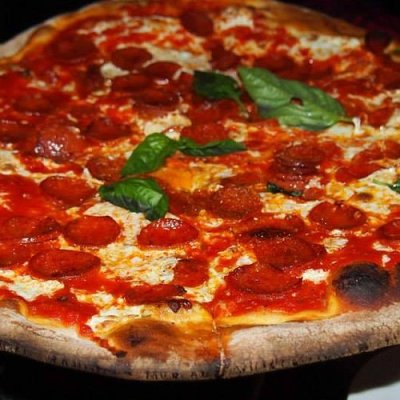 Thin-crust pizza topped with pepperoni, mozzarella, and basil, on a pizza stand.
