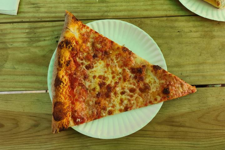 A slice of cheese pizza on a paper plate on a wooden table.