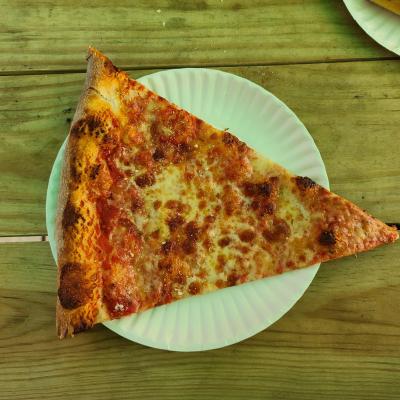 Slice of cheese pizza on a paper plate on a wooden table.