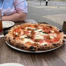 Wood-fired pizza with cheese and basil on a plate outdoors.