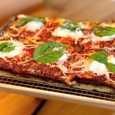 Close-up of a rectangular pizza with basil leaves and cheese on a wire rack.