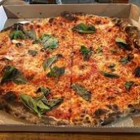 A pizza with cheese and basil leaves in a cardboard box.