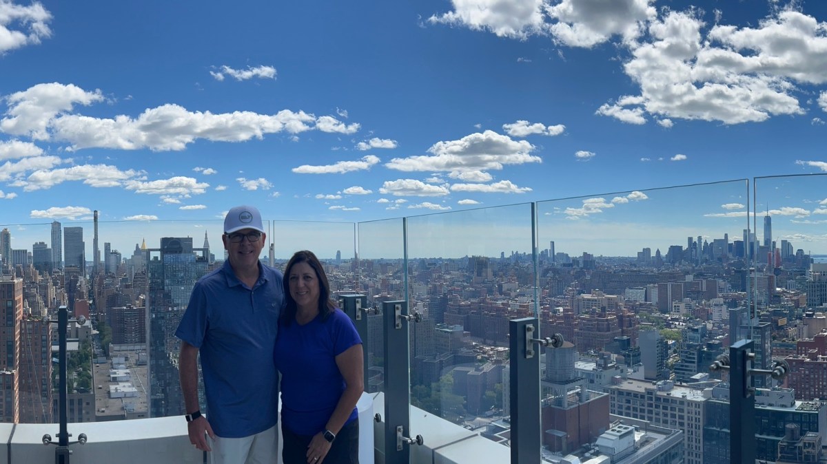 Two people standing on a rooftop with a city skyline view.