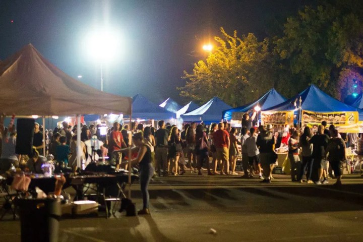 Crowd at night market with tents and lights, people shopping.