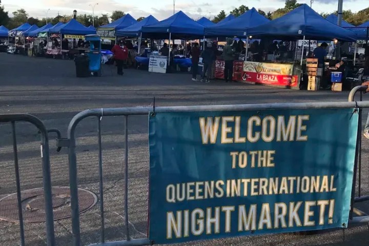 Outdoor market with blue tents and a sign saying 'Welcome to the Queens International Night Market!'