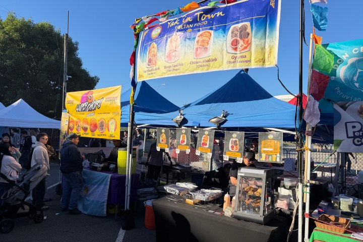 Food stalls at an outdoor market with people and colorful banners.