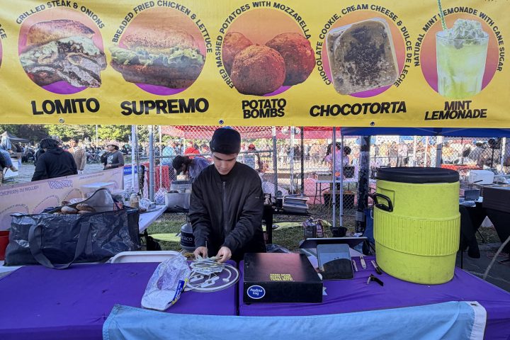Food stall with sandwich menu and Argentine flag on table.