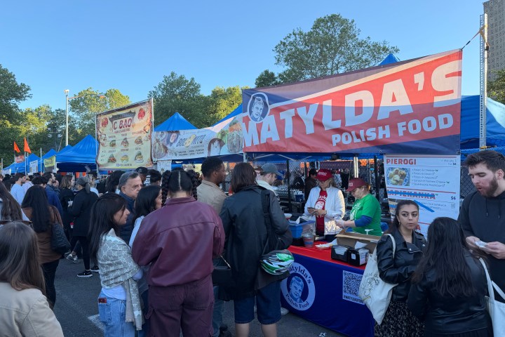 People at a food market near a Polish food stall with a banner.