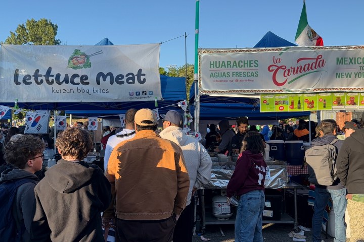 Outdoor food market with people in jackets, tents, and signs for Korean BBQ and Mexican food.