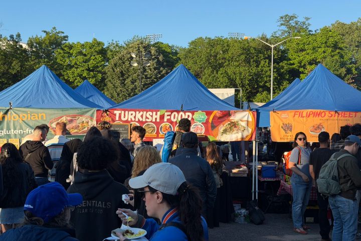 Crowd at outdoor food market with blue tents and various ethnic cuisine banners.