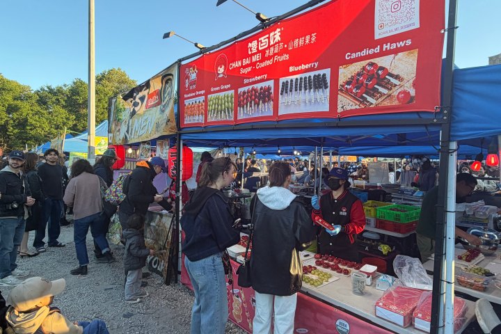 People at an outdoor market stall selling candied fruit with a red canopy.