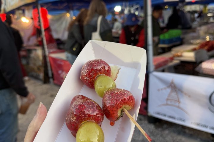 Hand holding candied fruit skewer at an outdoor market.